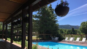 A wooden deck with a pool, white lounge chairs, and hanging flower baskets. - Fish Hook - Cozy cabin tucked in the mountains (Clark)
