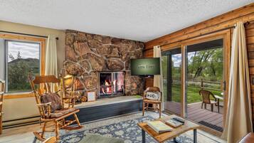 A cozy living room with a stone fireplace, comfortable seating, and a television.