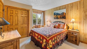 A bedroom with a large bed, two bedside tables, a wooden wardrobe, a window with a view of trees, and a painting on the wall. - Fish Hook - Cozy cabin tucked in the mountains (Clark)