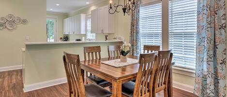 A dining area with a wooden table and chairs, a chandelier, and a window with blinds.