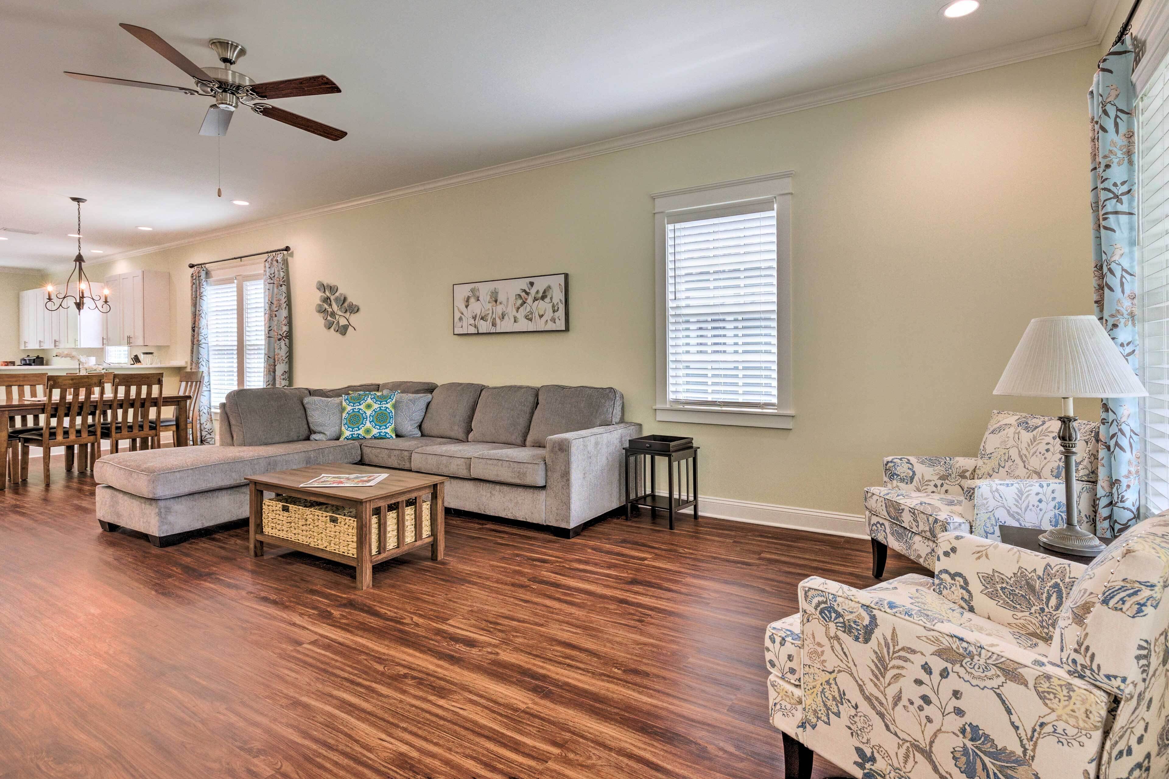A living room with a sectional sofa, a patterned armchair, a coffee table, and a ceiling fan.