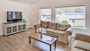Una sala de estar con un sofá, una mesa de centro, un televisor en un mueble y ventanas amplias.