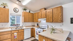 Una cocina moderna con armarios de madera, una estufa blanca y un ventanal con vista a árboles.