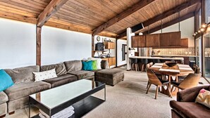 Amplia sala de estar con techo de madera, un juego de sofá, una mesa de comedor con sillas y una zona de cocina con armarios de madera.