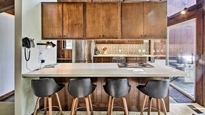 Una cocina moderna con armarios de madera, un refrigerador de acero inoxidable y una zona de bar con taburetes.