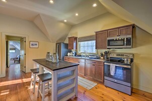 Una cocina con armarios de madera, horno de acero inoxidable, microondas e isla de madera con taburetes.