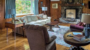 A cozy living room with a fireplace, wooden walls, a sofa, and a coffee table. - Chester Farmhouse on 100 Acres, 15 Min to Okemo! (Chester)