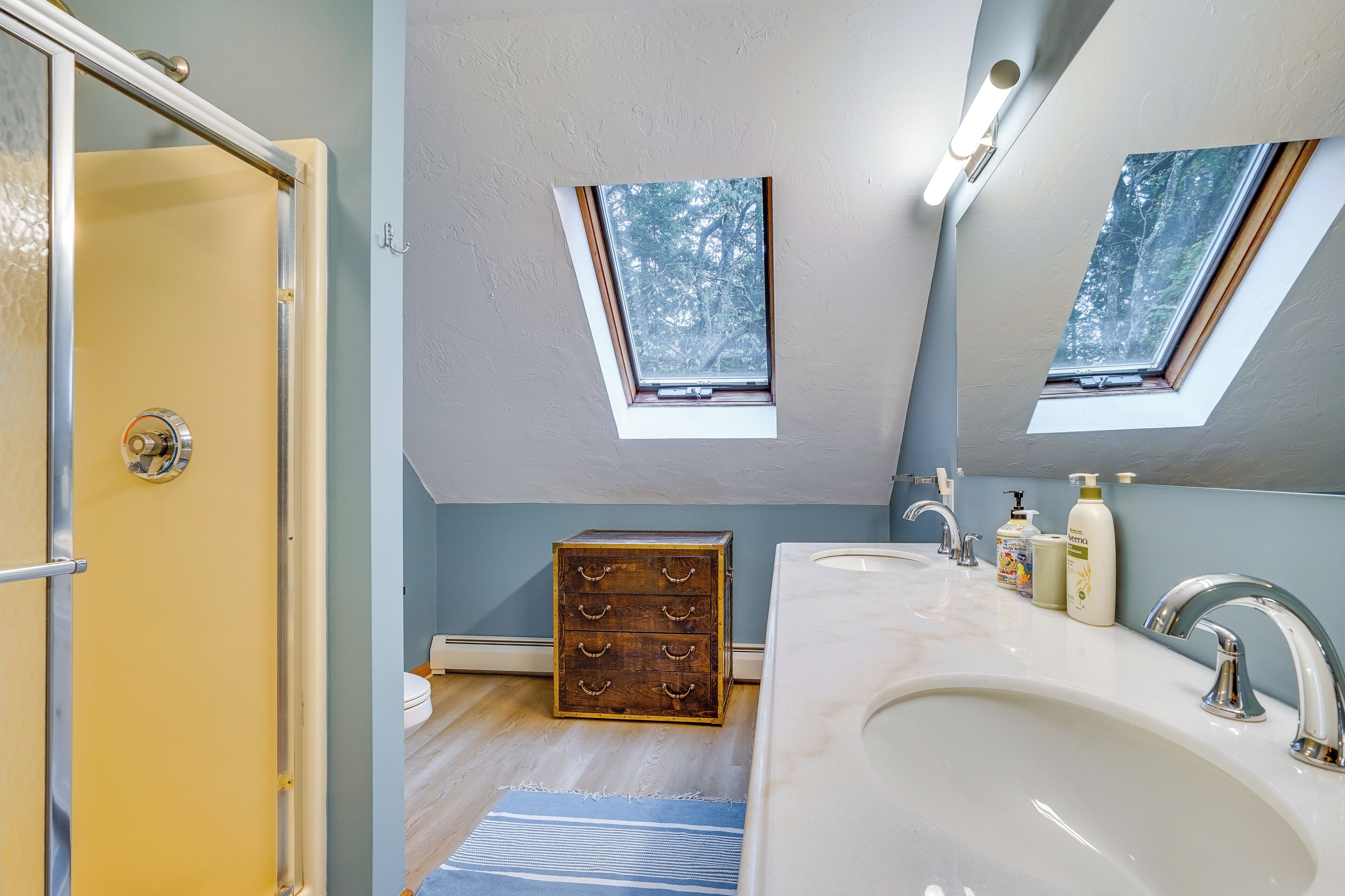 Un baño con tragaluz, un aparador de madera, un lavabo blanco y un espejo.