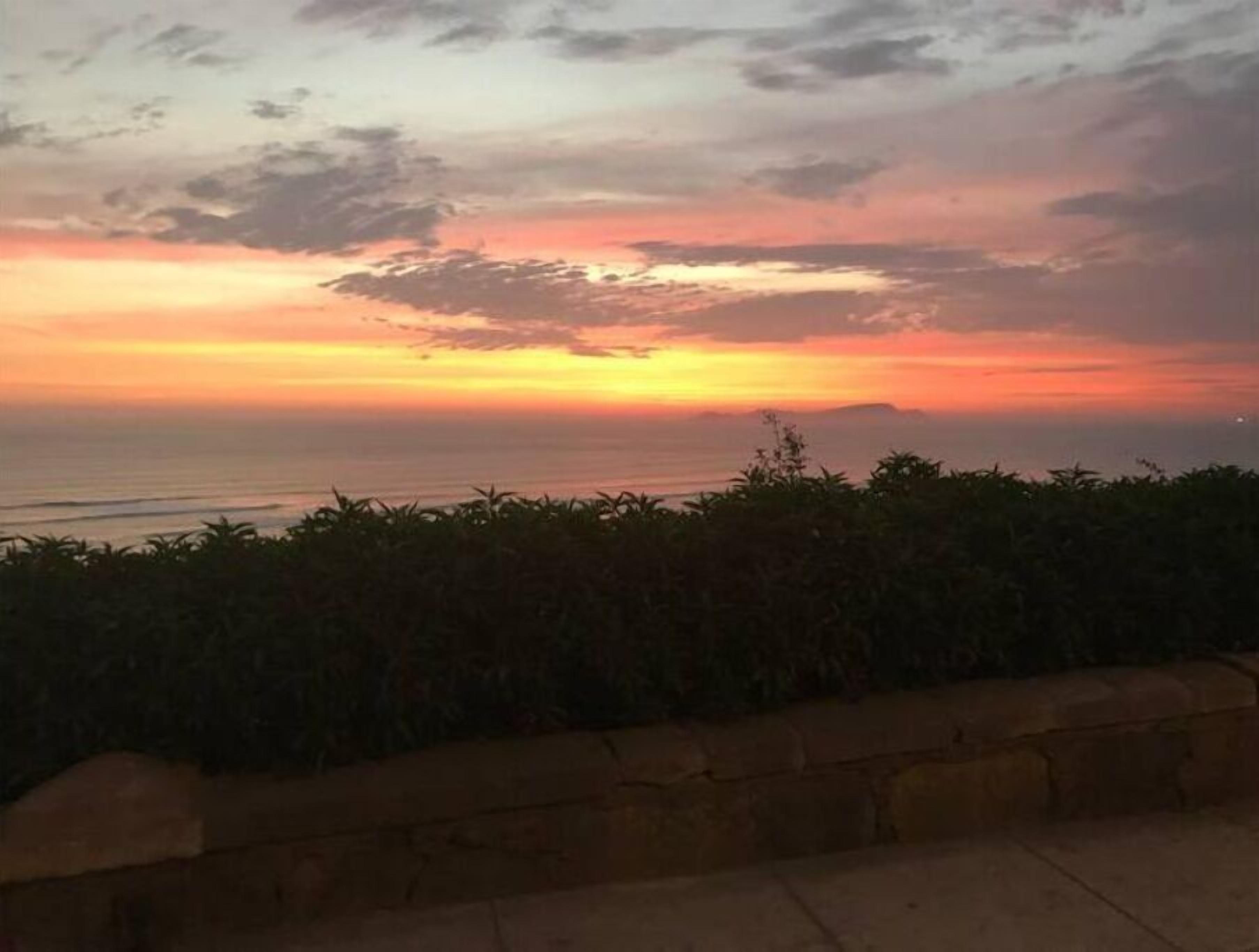 Ein Sonnenuntergang über dem Meer mit einer Steinmauer im Vordergrund.