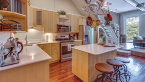 A modern kitchen with wooden cabinets, a central island with stools, stainless steel appliances, and a staircase leading to a loft area. - 'kentucky Bourbon Loft' ~ Downtown Louisville (Louisville)
