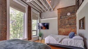 A bedroom with a large window, a flat-screen TV, and a bed with a gray blanket. - 'kentucky Bourbon Loft' ~ Downtown Louisville (Louisville)