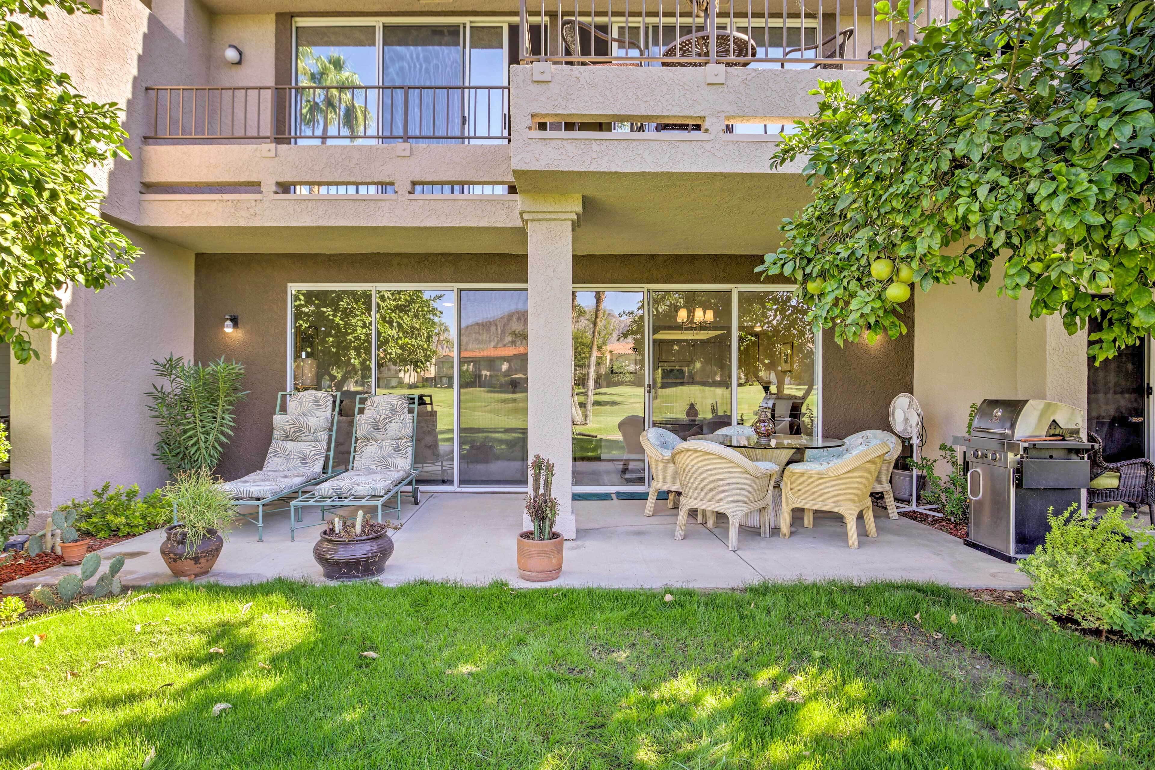 A two-story building with a patio area featuring outdoor furniture, a grill, and potted plants.