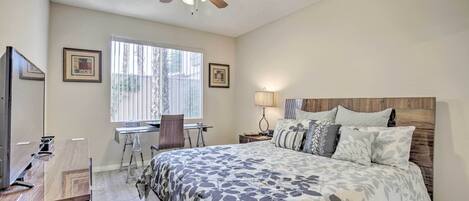 A bedroom with a bed, a desk, a chair, a ceiling fan, and a window.