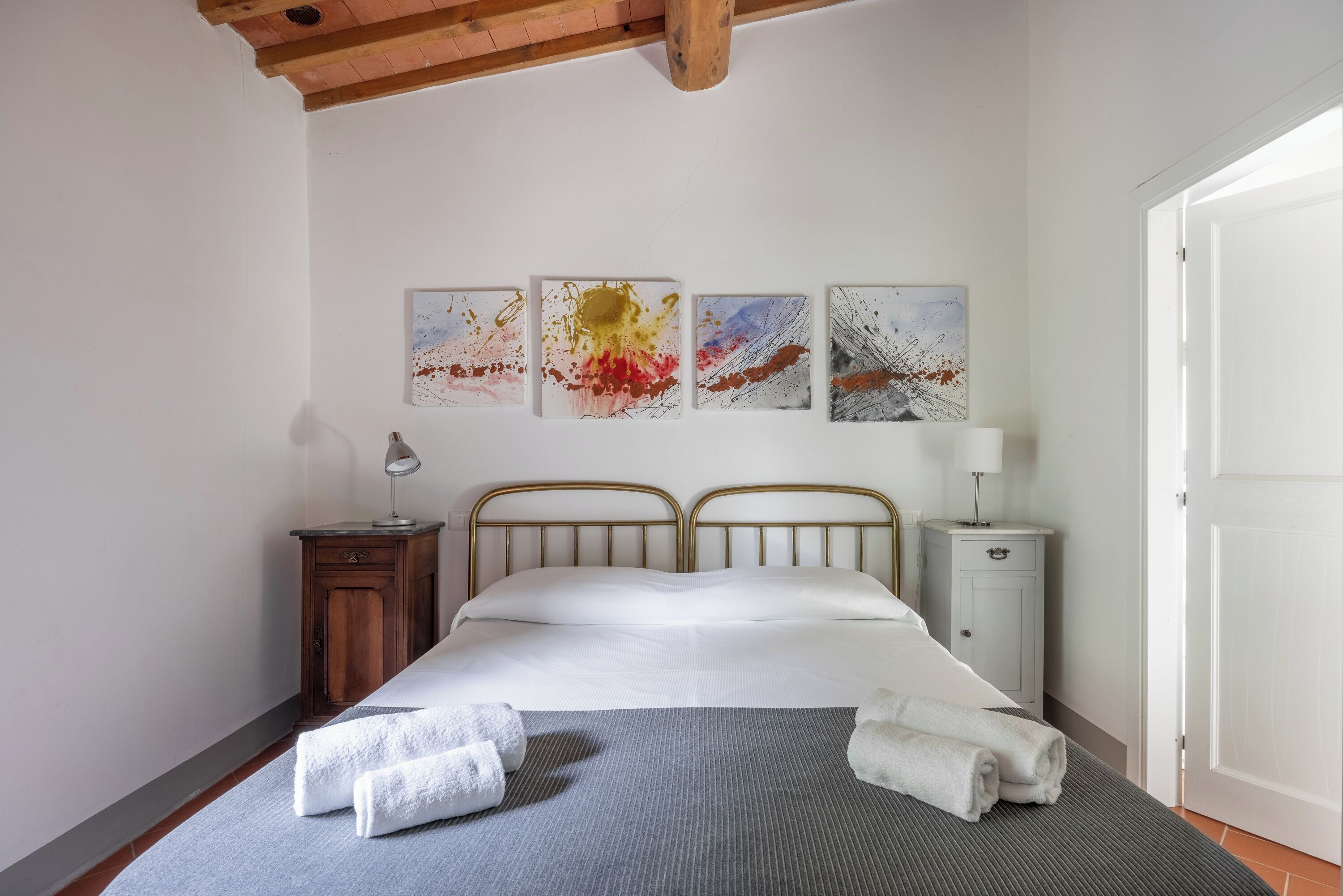 Un dormitorio con una cama, dos mesitas de noche, una mesilla auxiliar y cuatro cuadros abstractos en la pared.