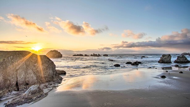 Uma praia com pedras grandes e águas calmas ao pôr do sol.