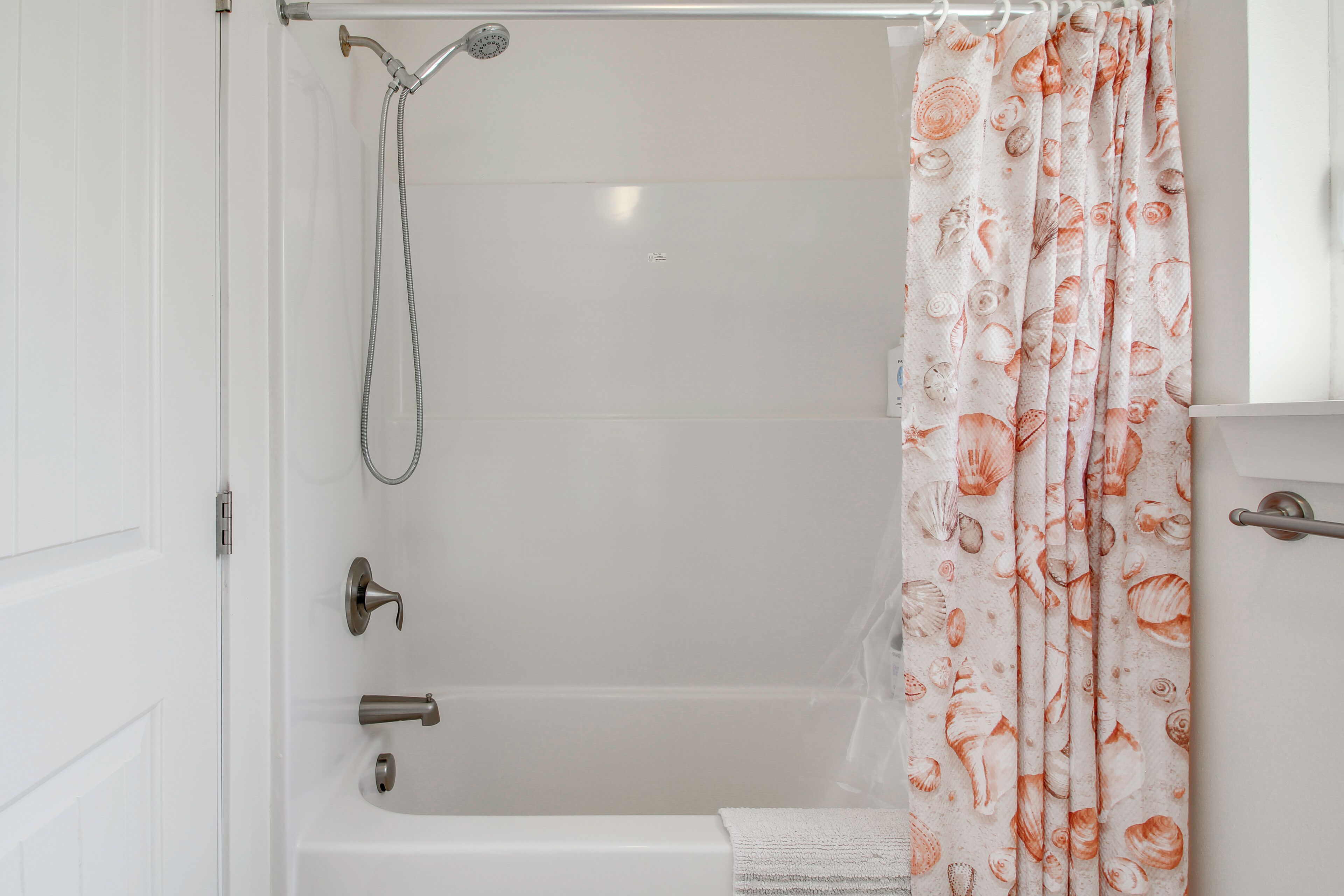A bathroom with a shower, a toilet, and a curtain with a shell pattern.