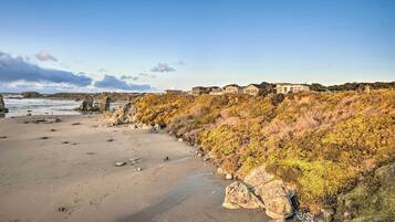 A coastal property with a sandy beach, rocky outcrops, and a hillside covered in autumn foliage.