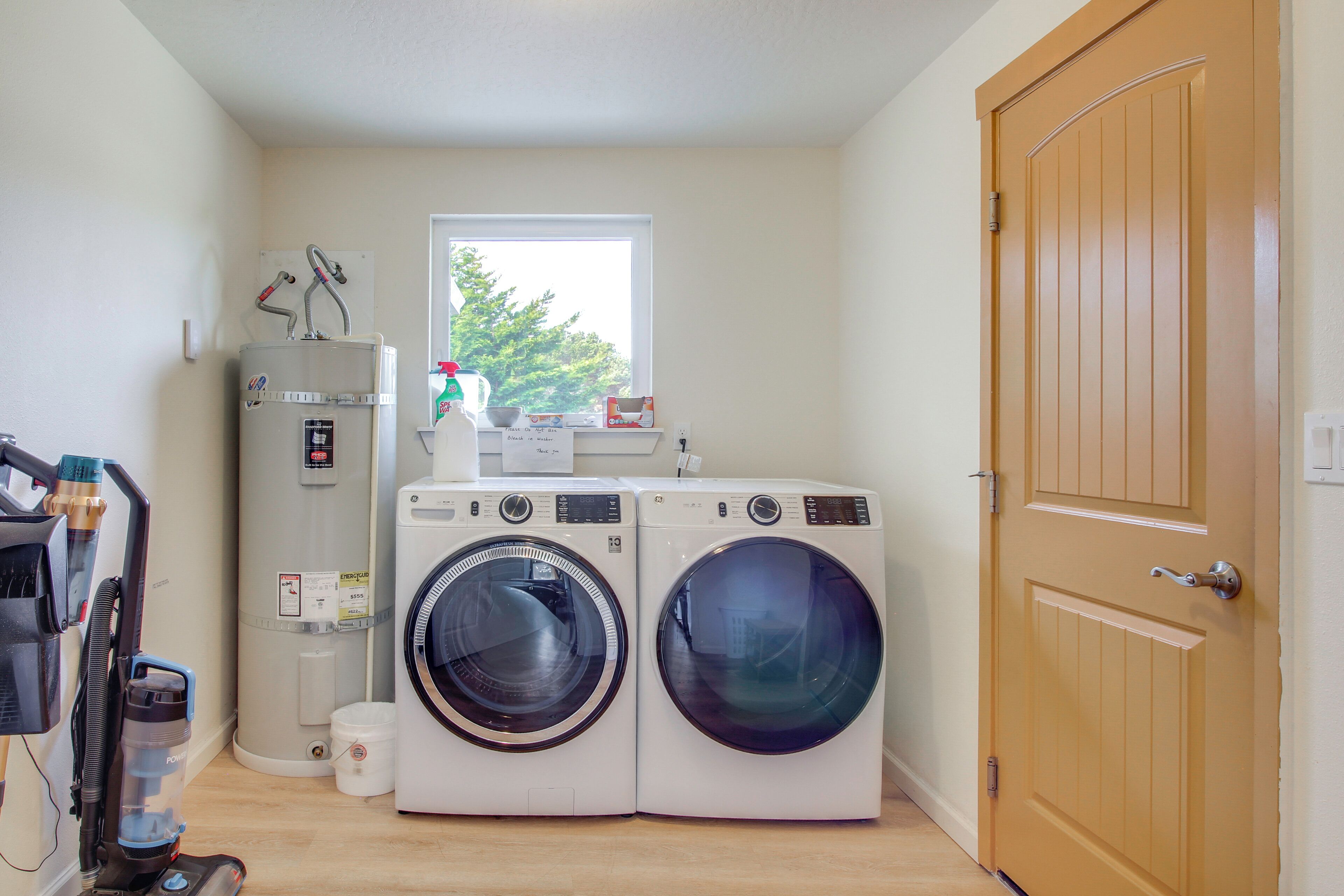 A laundry room with two front-loading washing machines, a water heater, and a vacuum cleaner.