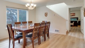 Uma sala de jantar com uma mesa e cadeiras de madeira, um candelabro e uma janela grande com persianas.