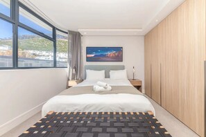 A modern hotel room with a large bed, a view of the city, and a painting on the wall.