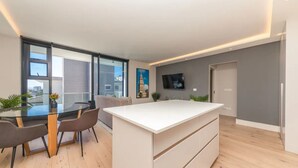 Cozinha moderna com ilha central, área de jantar com mesa de vidro e amplas janelas com vista para a cidade.