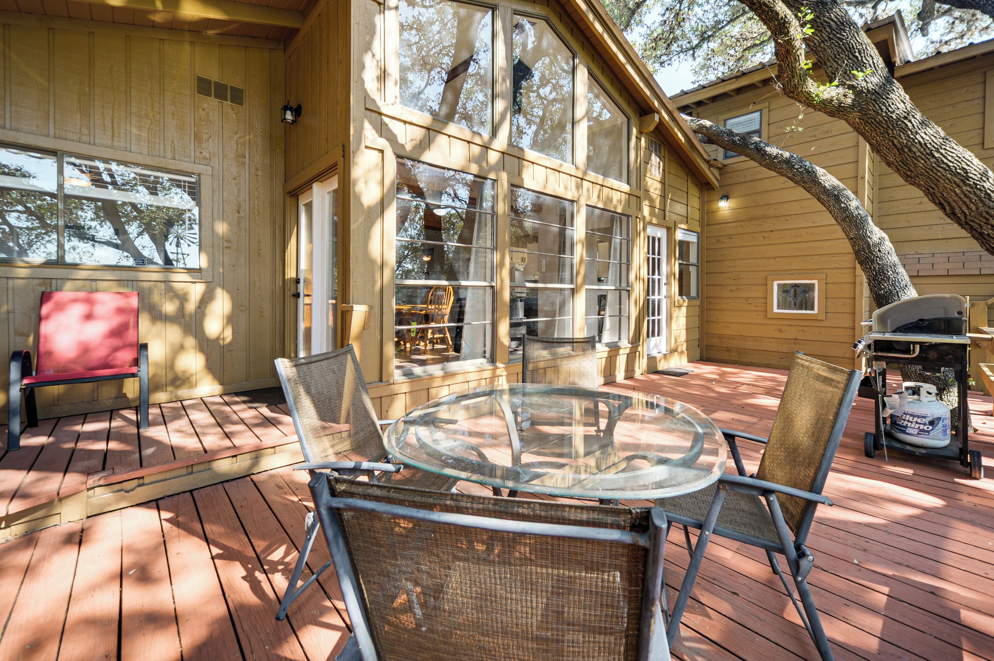 Une terrasse en bois avec une table et des chaises en verre, un banc rouge et un chariot-barbecue.