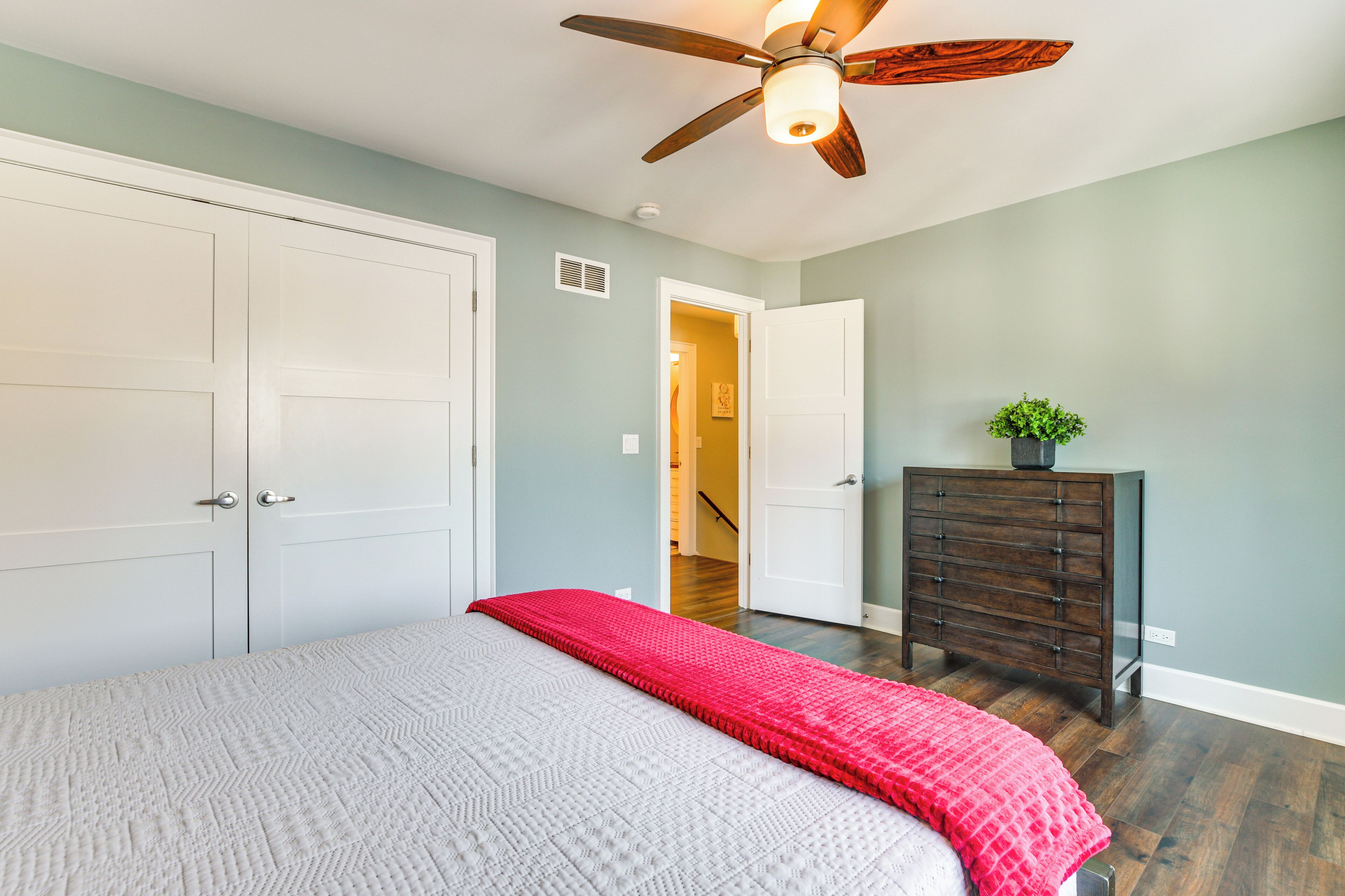 A bedroom with a bed, a ceiling fan, a dresser, and a hallway leading to another room.