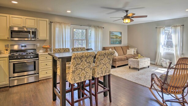 A modern kitchen with built-in appliances, a dining area with patterned chairs, a ceiling fan, and a living room with a sofa and ottoman. - Stylish Pine Plains Home Near Parks & Hiking! (Pine Plains)