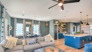 Una sala de estar moderna con un sofá gris, un reposapiés azul y una isla de cocina con armarios azules.