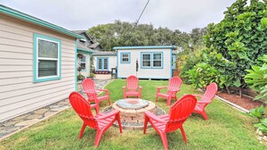 Un giardino sul retro con un braciere, sedie rosse, una casa con decorazioni blu e un'area coltivata con diverse piante.