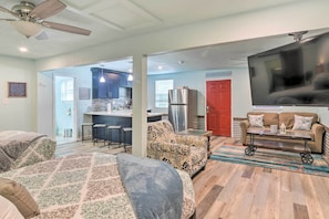 A spacious living room with a sofa, a coffee table, and a TV. There is a kitchen area with a refrigerator and a dining table.