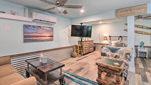 Un soggiorno con una ventola a soffitto, una televisione a schermo piatto, un divano, un tavolino da caffè e un cartello con scritto "Beach House".