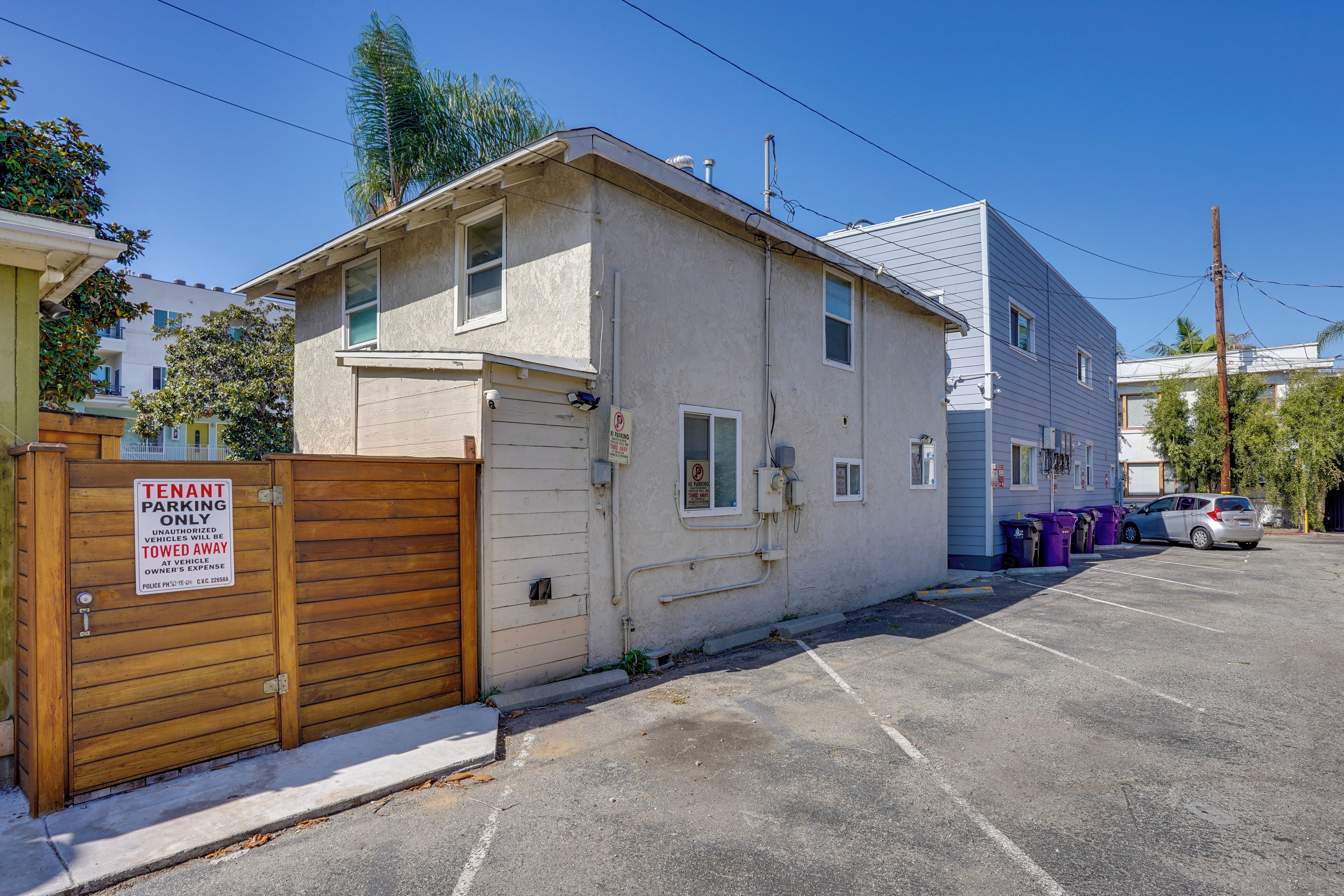 A two-story building with a gated entrance, a parking lot, and a row of parked cars.