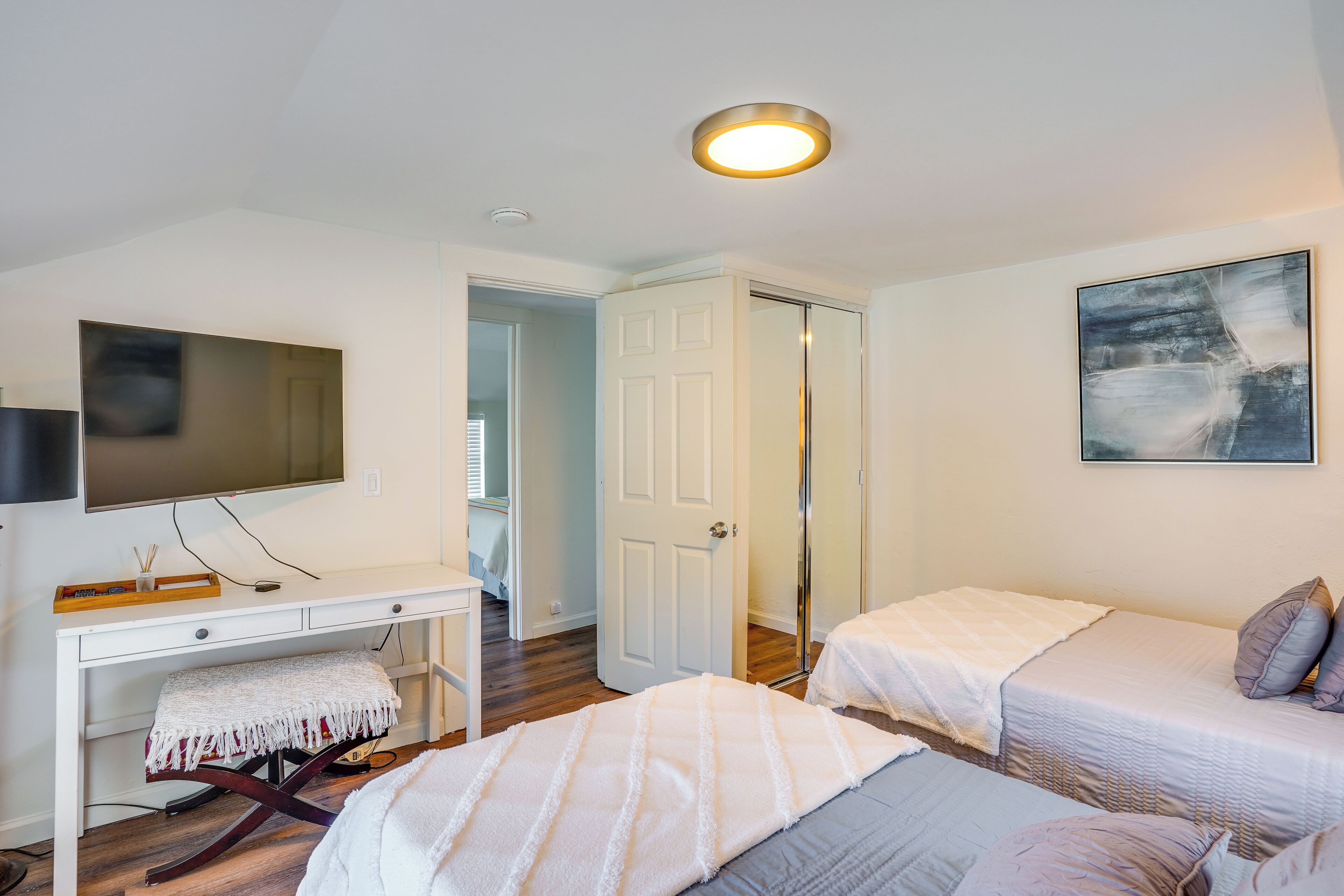 Een slaapkamer met twee bedden, een bureau, een televisie en een deur naar een andere kamer.