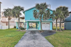 Une maison turquoise à deux étages, dotée d’un porche abrité, de palmiers et d’un garage.