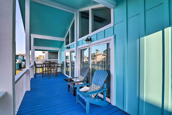 Une véranda couverte avec un plancher bleu et des balustrades blanches, agrémentée de deux fauteuils Adirondack et d’une petite table.