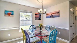 A dining area with a glass table surrounded by colorful chairs, a chandelier, and artwork on the walls.