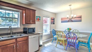 A kitchen with wooden cabinets, a dishwasher, a microwave, and a dining area with colorful chairs and a table.