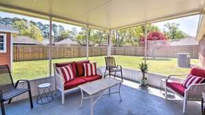 A covered patio with a red and white striped sofa, two wicker chairs, and a small table.