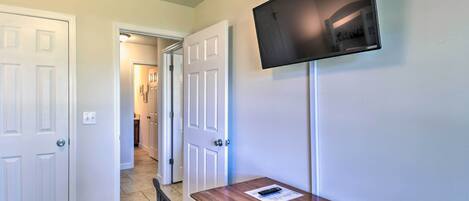A room with a wooden desk, a mounted flat-screen TV, and a door leading to a hallway.