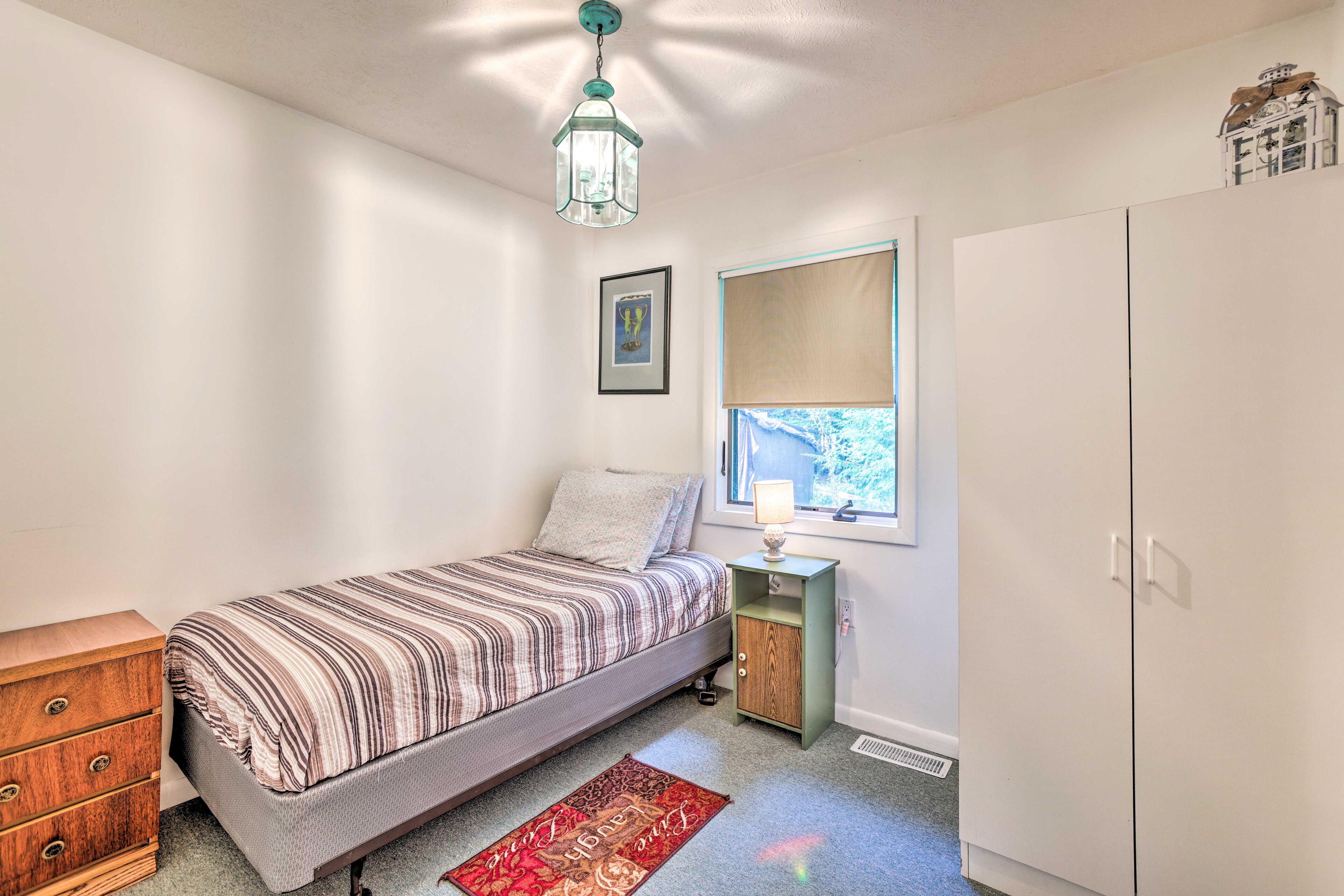 A bedroom with a bed, dresser, nightstand, lamp, window, and wardrobe.