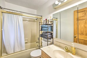A bathroom with a glass-enclosed shower, a toilet, a sink with a mirror, and a wooden door.