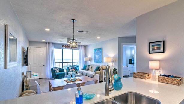 A modern kitchen with a large island, stainless steel sink, and a dining area with a table and chairs. - Ocean-view Balcony: Family Gem on Seawall Blvd! (Galveston)