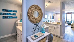 A modern kitchen with white cabinetry, a central island, and a dining area with a view of the living room. - Ocean-view Balcony: Family Gem on Seawall Blvd! (Galveston)