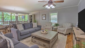 A spacious living room with a gray sofa, striped armchairs, a wooden coffee table, and a ceiling fan. - The Lake Escape: Boat Dock, Fire Pit, Kayak! (Cropwell)