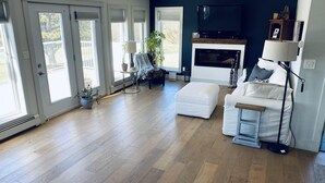 Ein geräumiges Wohnzimmer mit Holzdielen, einem weißen Sofa, einem kleinen Tisch und einem Fernseher über einem Kamin.
