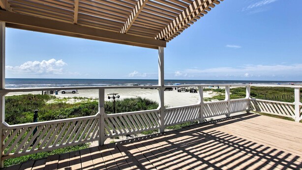 A wooden deck with a white railing overlooking a beach with vehicles and a clear sky. - Galveston Beachfront House w/ Deck & Ocean Views! (Galveston)