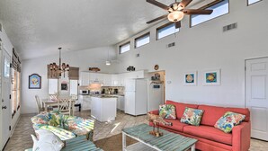 A spacious living area with a red sofa, a coffee table, and a dining table with chairs. There is a kitchen in the background with white cabinets and a refrigerator. - Galveston Beachfront House w/ Deck & Ocean Views! (Galveston)