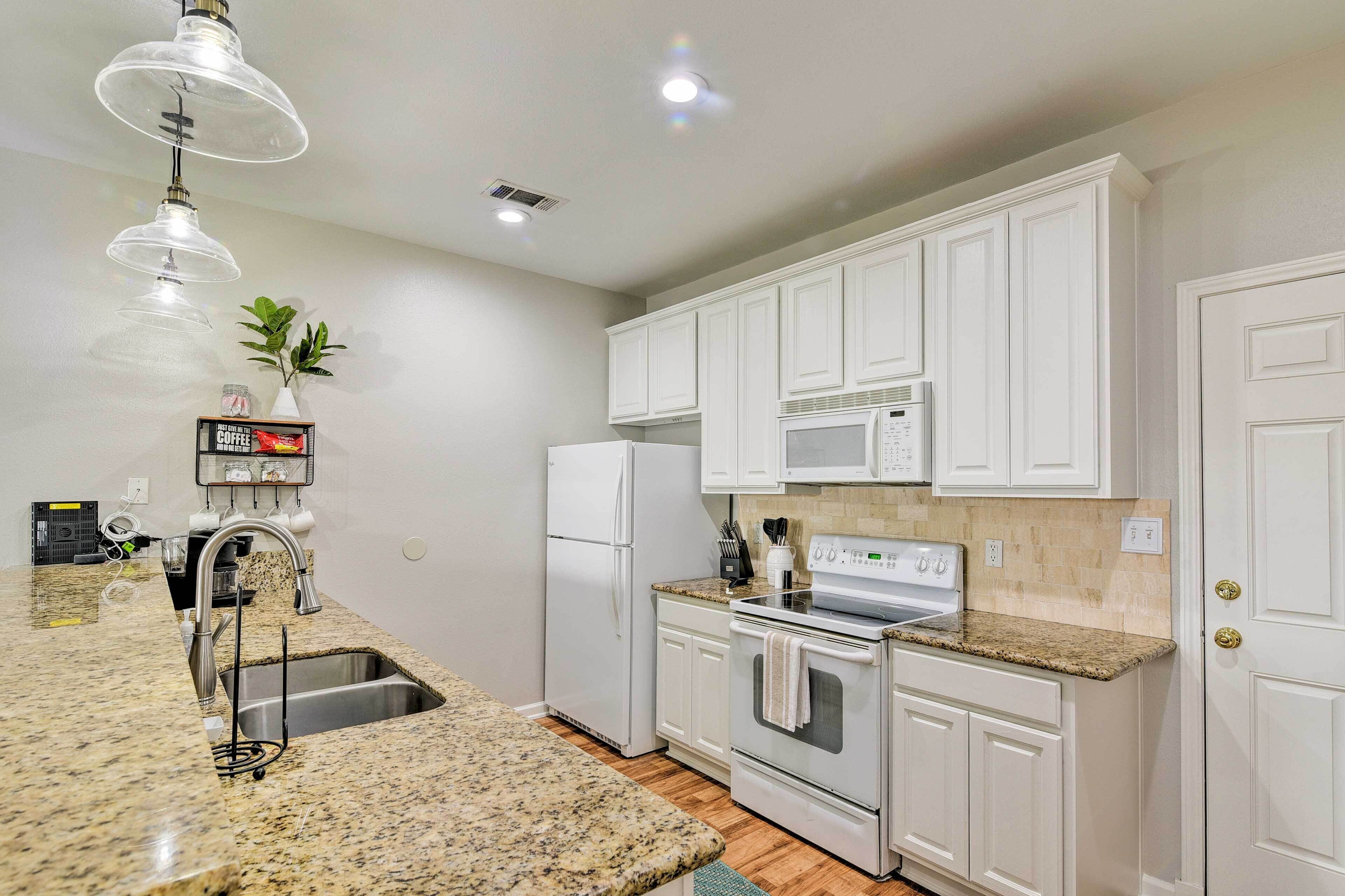 A modern kitchen with white cabinets, a granite countertop, stainless steel appliances, and pendant lighting.