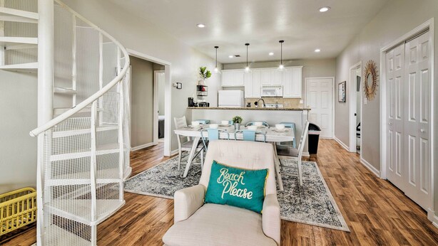 A spacious living area with a staircase, a dining table, and a kitchen in the background.